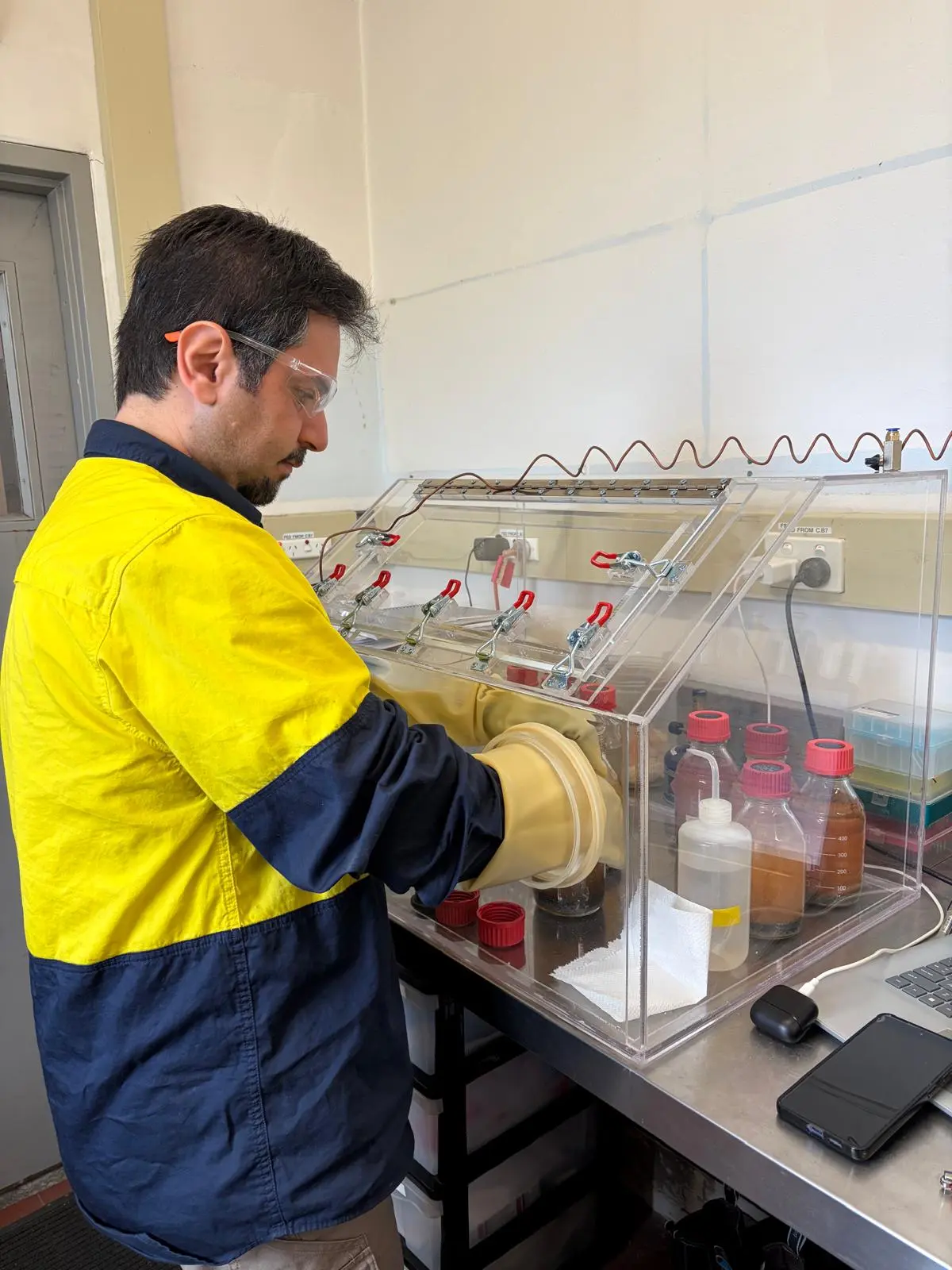 Reseacher handling sample bottles inside glove box for groundwater bioremediation testing.
